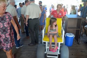 Flagler Beach Commission Chairman Jane Mealy shows off the beach-access chair for the handicapped (the child was just taking a ride), with Kim Tilly to the left. Click on the image for larger view. (© FlaglerLive)