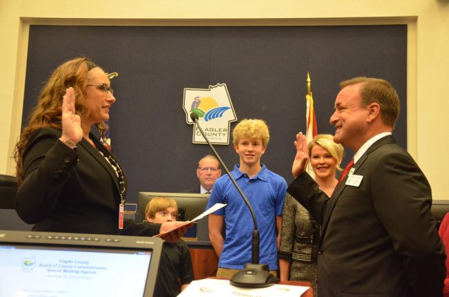 County Judge Melissa Moore-Stens swears-in Joe Mullins in front of his family and, on the dais, Greg Hansen, who was also sworn-in to his first full term today. Click on the image for larger view. (© FlaglerLive)