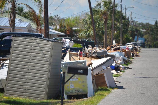 Palm Circle in Flagler Beach is now a wall of discarded belongings stretching as far as the eye can see, and blocking the view in front of every single house. The scene is repeated along many streets in Flagler Beach, to a far greater extent than in the first few days after Hurricane Irma plowed through the region. Click on the image for larger view. (© FlaglerLive)