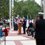 Palm Coast Fire Chief Jerry Fortye speaking at last year's September 11 ceremony at heroes Park, with the seedling grafted from the Sept. 11 tree, to the left. (© FlaglerLive)