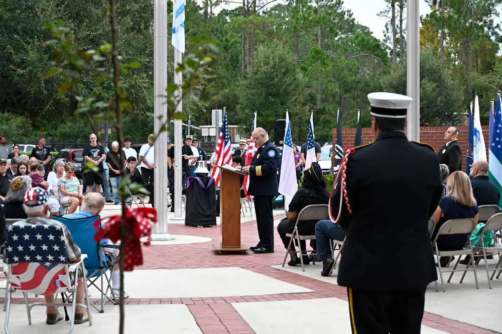 Palm Coast Fire Chief Jerry Fortye speaking at last year's September 11 ceremony at heroes Park, with the seedling grafted from the Sept. 11 tree, to the left. (© FlaglerLive)