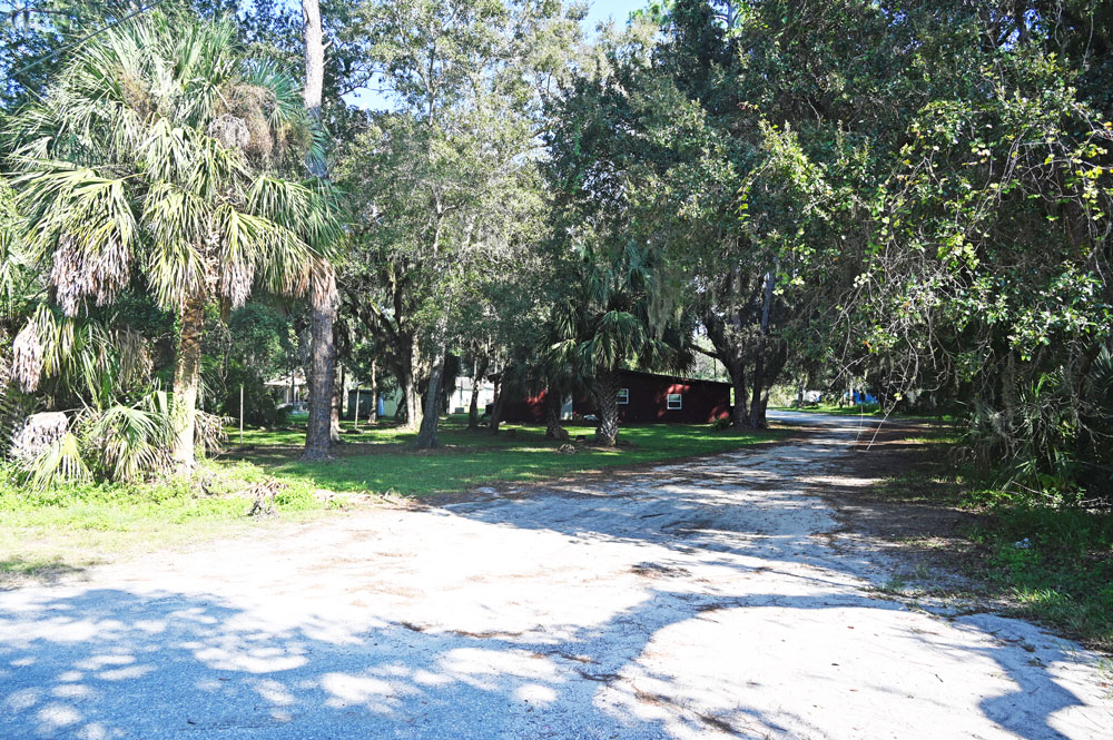 The land and trees to the left of the road, as well as the road, are part of the county's Espanola Park. St. Paul Baptist Church--the red-brick building--wants to but the tree-shaded land to the left, level it, and build a parking lot there. The county was ready to accommodate it. Without a bid. (© FlaglerLive)