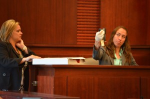 Maria Pagan, a crime lab analyst with the Florida Department of Law Enforcement, hoisted the 9 mm semi-automatic Paul Miller used to fire five bullets at Dana Mulhall. Assistant State Attorney Jacquelyn Ros is to the left. Click on the image for larger view. (© FlaglerLive)