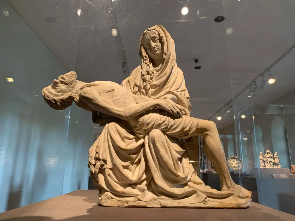 A limestone sculpture of Mary and Christ  believed to date from around 1400, possibly from Prague, and now part of the Metropolitan Museum's Cloisters Collection. The accompanying note reads: "Christian scripture does not mention a moment when Jesus' mother held his deceased body in her lap. Nonetheless, in the hands of theologians and then artists, this imagined moment became the focus of prayer and reflection. Here, the sculptor sets the emaciated, almost naked body of Jesus against the ample, enveloping robes of Mary, who grasps his thin wrist as if to check his pulse. The sculpture's poignancy surpasses the boundaries of Christianity to touch a nerve about the love of a mother for her son and the tragedy of an early death." (© FlaglerLive) 