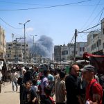 Palestinians crowd a street as smoke billows from Israeli strikes in Rafah on May 7, 2024.