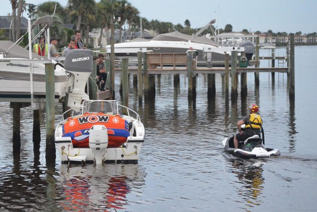 Responders from various local and state agencies were leading the search from the dock at 234 Ocean Palm Drive in Flagler Beach. The boat the 20-year-old victim was riding, with its large orange tube, was docked below the rescuers. (© FlaglerLive)