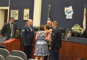 County Commissioner and Chairman Barbara Revels hugs Debbie Meeker at the end of a tribute to Frank Meeker, with the late commissioner's sons Josh and Jason, and County Administrator Craig Coffey, standing by. <br /><figcaption id=