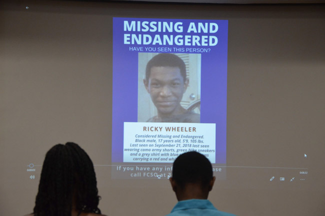At a celebration of the search that led to his find, Ricky Wheeler and his mother sat in front of the projection of his own missing-person flier that was disseminated when he went missing on Sept. 21. (© FlaglerLive)