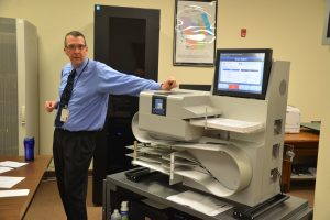 Ryan Kramer and the scanning machine that processes 300 ballots a minute. He is standing in front of the office's server, in the black box to the rear.  Click on the image for larger view. (© FlaglerLive)