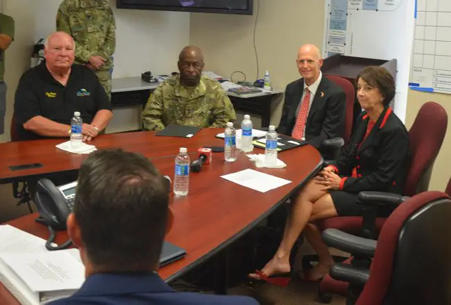 Gov. Rick Scott, second from right, speaking with local officials in a closed-door meeting Monday afternoon at the county's Emergency Operations Center, including, from left, Palm Coast Mayor Jon Netts, Adjutant General of Florida Maj. Gen. Michael Calhoun, and County Commission Chairman Barbara Revels. Their eyes are on County Administrator Craig Coffey. (© FlaglerLive)
