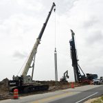The drill at right that creates the 18- and 36-ft. holes, filling them with concrete, before reinforced rebar (the cylindrical object in the center) is pushed through the concrete, forming a segment of the secant wall. Workers were on the job in Volusia County's portion of the wall today. Flagler County's wall is nearly complete. (© FlaglerLive)