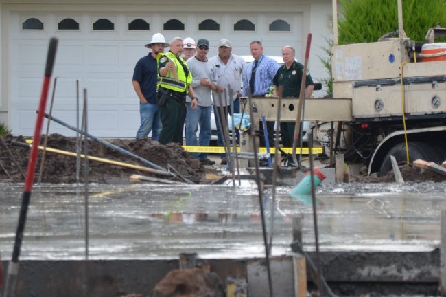 The sheriff getting briefed at the scene this morning.. The bodies of the two workers were within a few feet to the left of the group, covered in white sheets. (© FlaglerLive)