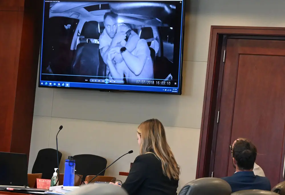 Travis Smith, flanked by his two attorneys, watches himself in footage of his attack on Nihat Aksezer at the aborted end of a Lyft ride Aksezer was giving Smith, his friend and his friend's son in Palm Coast two years ago. Smith is on trial over that attack. (© FlaglerLive)