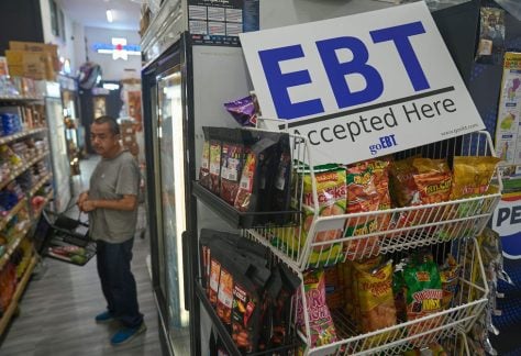 A man shops at El Recuerdo Market in Los Angeles in 2025, next to a sign indicating that customers may pay with SNAP benefits.