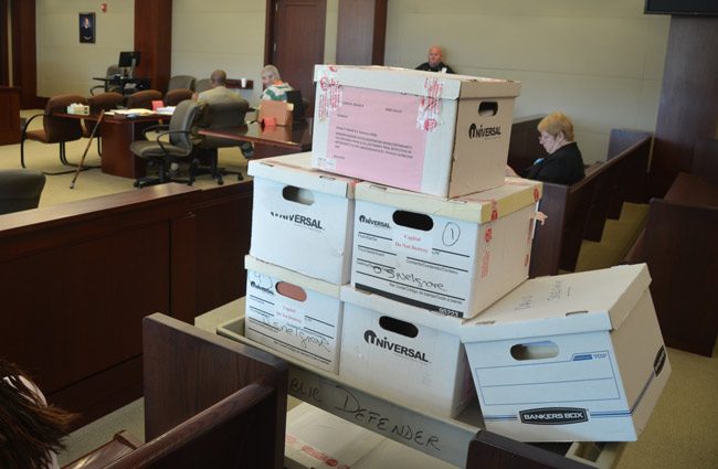 Some of the 20-odd boxes in David Snelgrove's murder case, brought in when he was last in court in 2015. He is seen in the striped green and white overalls in the distance. He was not in court today, but is scheduled to be in court in October for the next phase of his case, which has meandered through court since 2000. (© FlaglerLive)