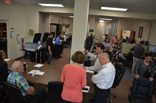 Members of the canvassing board and alternates are in the foreground, spectators are to the right, the machines to the left. (c FlaglerLive)