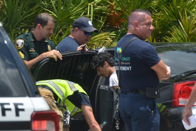 Levi Evan Ovenshire, the 19-year-old suspect, in the center of the picture, as he was being checked out by paramedics soon after his arrest on Rae Drive this afternoon. Click on the image for larger view. (© FlaglerLive)