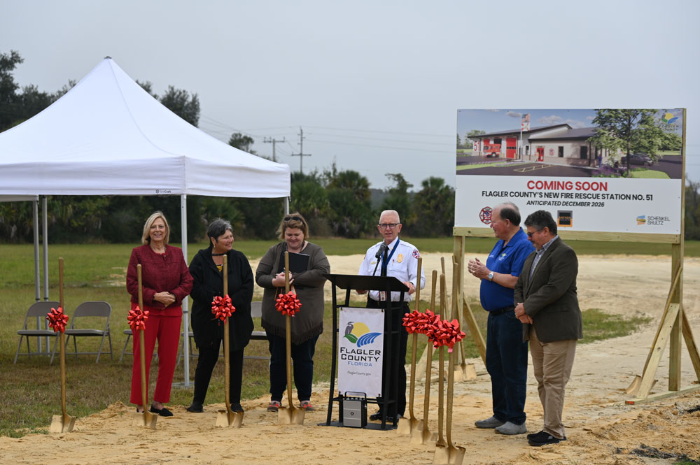 Fire Chief Michael Tucker addressing the crowd his morning, with a rendering of the new station behind him. (© FlaglerLive)
