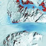 A satellite image shows the long flow lines as a glacier moves ice into Antarctica’s Ross Ice Shelf, on the right. The red patches mark bedrock. (USGS)