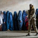 A Taliban fighter stands guard as women wait to receive food rations distributed by a humanitarian aid group in Kabul, Afghanistan, on May 23, 2023.