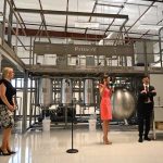 Vidya Herbs founder Kodimule Shyam Prasad, right, with state Commerce Secretary Laura DiBella, with the mic, and Helga van Eckert, who heads Vidya Herbs's Florida operations, at today's launch next to the company's state-of-the-art extractor. (© FlaglerLive)