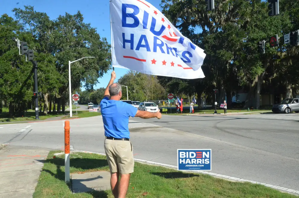 Peter Wentworth waving a Biden-Harris flag on Palm Coast Parkway on Election Day, across the street from Trump supporters. (© FlaglerLive)