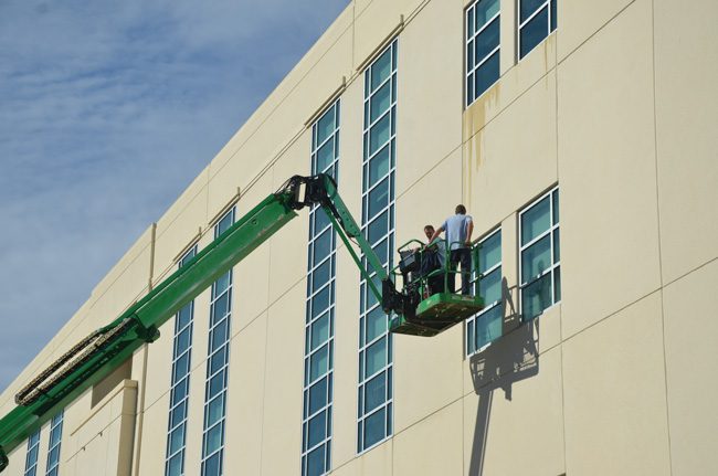 It takes a boom to keep those Flagler County courthouse windows clean: workers on Monday on the south facade of the building. (c FlaglerLive)