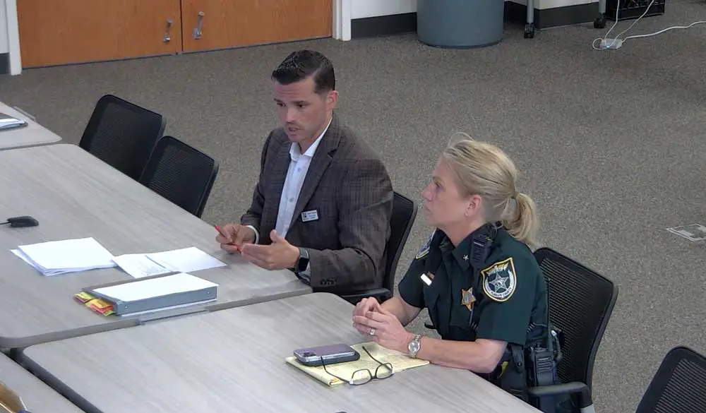 Tommy Wooleyhan, the Flagler County school district's safety specialist, discussing the potential of arming school staffers this afternoon before the Flagler County School Board, with the Sheriff's Office's Commander Jennifer Nawrocki. (© FlaglerLive via Flagler schools TV)