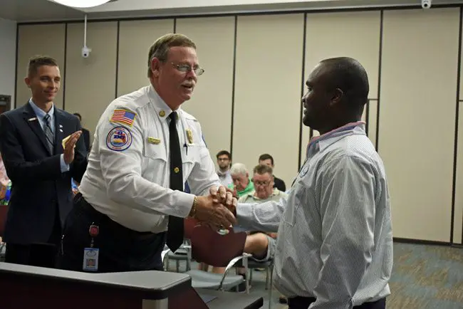 Palm Coast Fire Chief Mike Beadle, center, congratulates Brice Wright, a city utility employee, who was recognized with a proclamation Tuesday evening for helping victims of a vehicle crash in mid-June. Read the full proclamation here. (Cindi Lane)